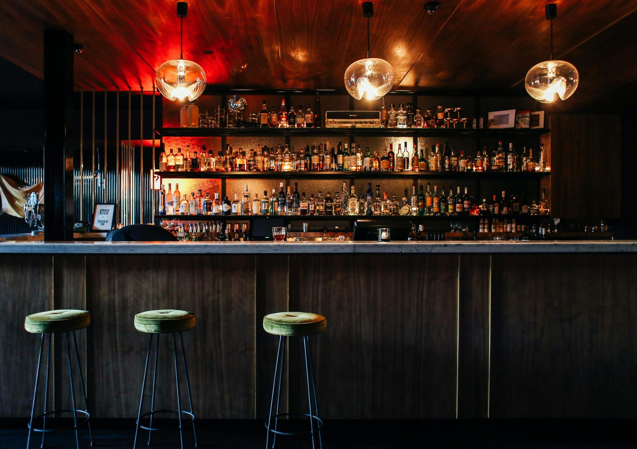Photo of a dimly lit bar with three empty bar stools.
